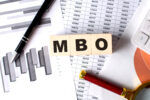 MBO text on wooden block on graph background with pen and magnifier